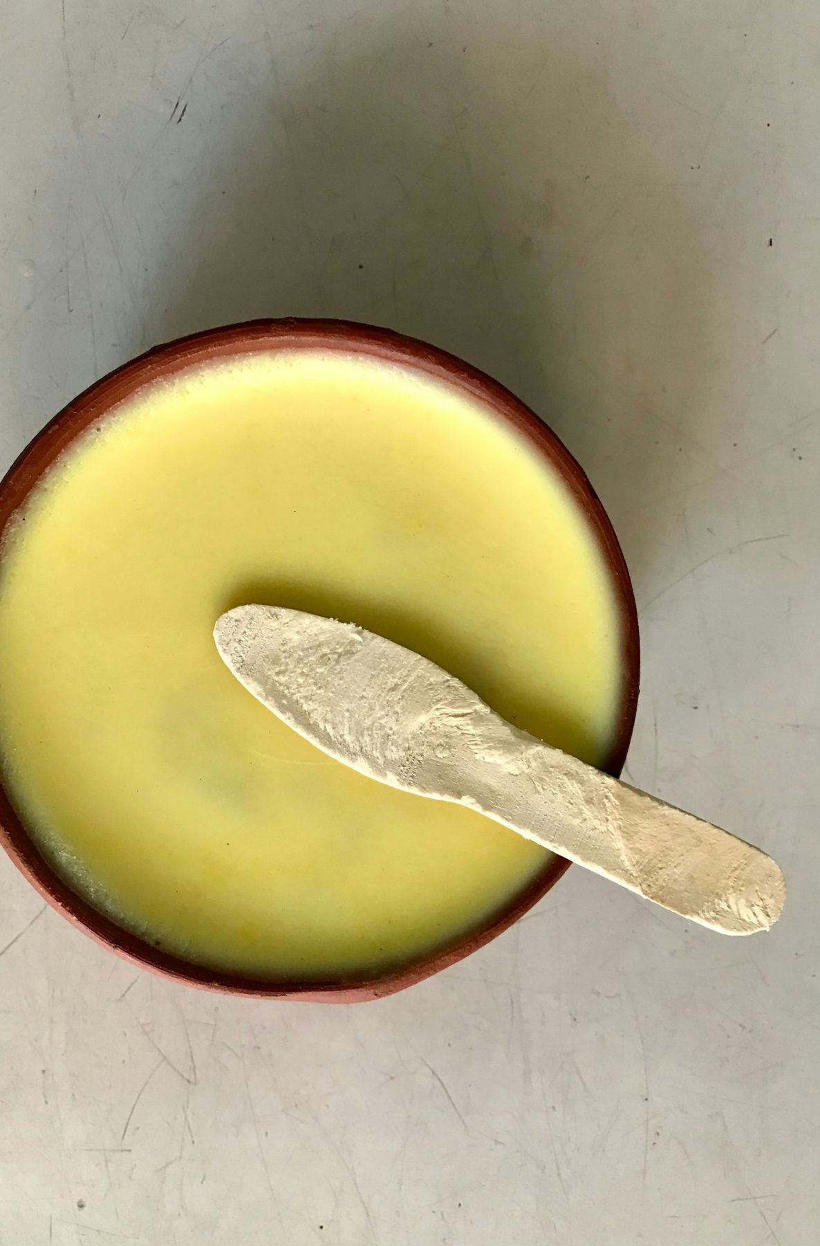 Ghee in a clay bowl with a wooden spreader